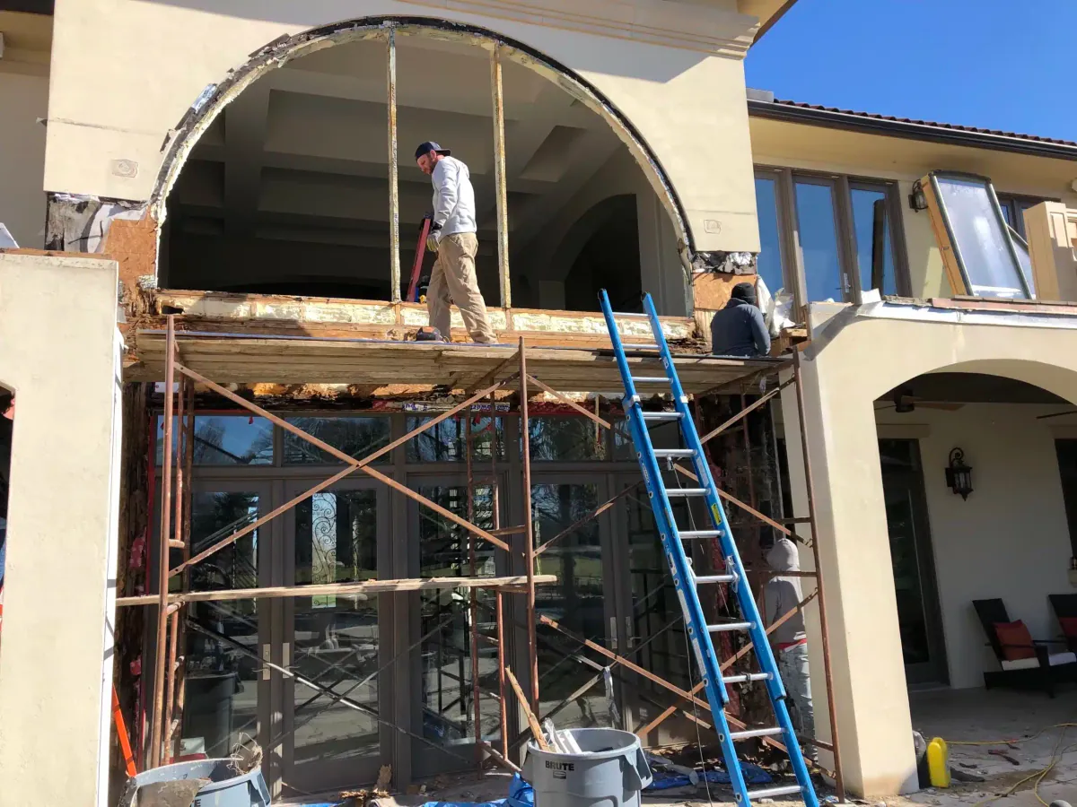 Scaffolding on a stucco home while the arched entry is prepared for new doors